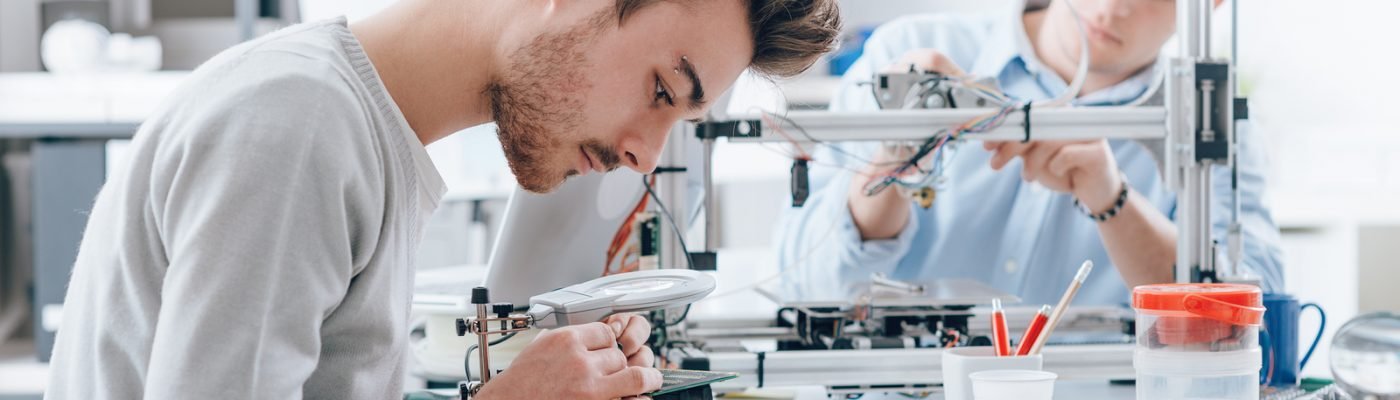 Engineering students working in the lab a student is using a voltage and current tester another student in the background is using a 3D printer